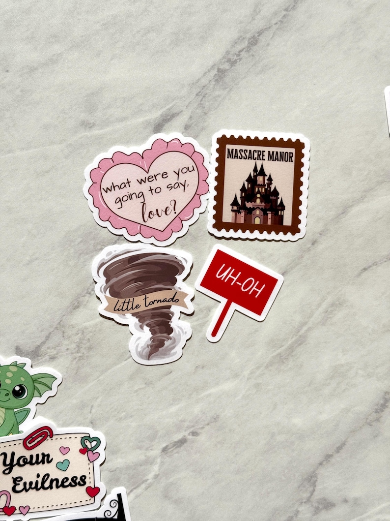 Puede incluir: Una colecci&oacute;n de pegatinas con varios dise&ntilde;os. Una pegatina es un coraz&oacute;n rosa con el texto "what were you going to say, love?". Otra es un sello marr&oacute;n con un castillo y las palabras "MASSACRE MANOR". Otras pegatinas incluyen un tornado y un letrero rojo que dice "UH-OH".
