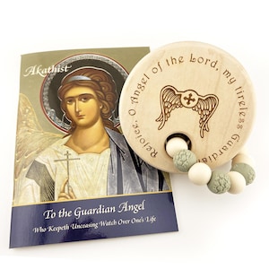 May include: A wooden baby rattle with a cross and angel wings design, and a book titled "To the Guardian Angel". The rattle has a string of white and green beads. The book has an illustration of an angel.