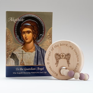 May include: A wooden baby rattle with a circular design featuring an angel with wings and a cross. The rattle has a quote in English: "Rejoice, O Angel of the Lord, my tireless Guard". The rattle is accompanied by a small book with a picture of an angel on the cover. The book's title is "Akathist to the Guardian Angel".