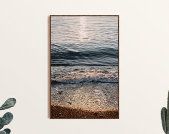 May include: A framed photograph of a beach scene with blue water and white waves crashing on the shore. The sand is a light brown color and the water is reflecting the sunlight.