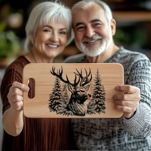 May include: A wooden cutting board with a black and white illustration of a deer in a forest setting. The board has a handle on the side.