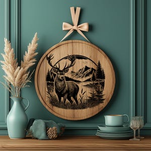 May include: A round wooden wall decor with a black and white illustration of a deer standing in a forest scene. The deer is in the center of the image and is surrounded by trees, a lake, and mountains. The background is a light brown color.