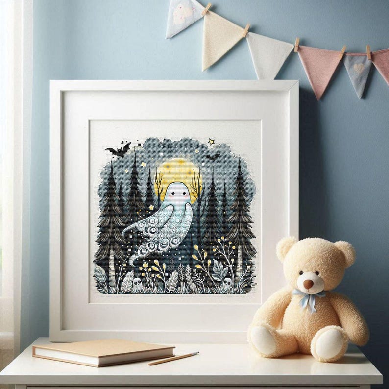 May include: A framed cross-stitch artwork featuring a whimsical ghost in a forest setting under a full moon. The artwork is in a white frame and includes bats, stars, and stylized trees. A teddy bear sits nearby.