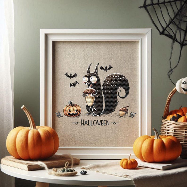 May include: A framed Halloween-themed cross-stitch featuring a black squirrel holding an acorn, with bats and pumpkins. The word "HALLOWEEN" is below the squirrel. Orange pumpkins and a basket of pumpkins are on a table.