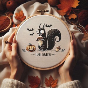 May include: A Halloween-themed cross-stitch embroidery hoop featuring a black squirrel holding an acorn, a jack-o'-lantern, and bats. The word "HALLOWEEN" is stitched below the squirrel. The embroidery is set in a wooden hoop, surrounded by autumn leaves.