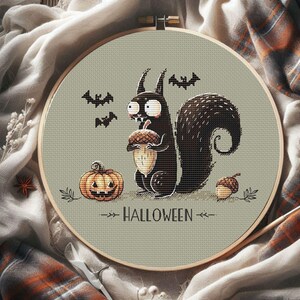 May include: A cross-stitch embroidery hoop featuring a Halloween design. A black squirrel holds an acorn, with a jack-o'-lantern, bats, and the word "HALLOWEEN". The design is set against a light green background, framed by a wooden hoop.