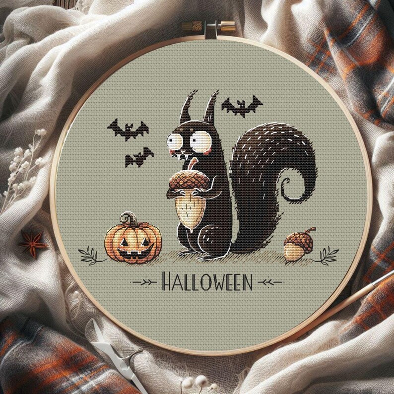 May include: A cross-stitch embroidery hoop featuring a Halloween design. A black squirrel holds an acorn, with a jack-o'-lantern, bats, and the word "HALLOWEEN". The design is set against a light green background, framed by a wooden hoop.