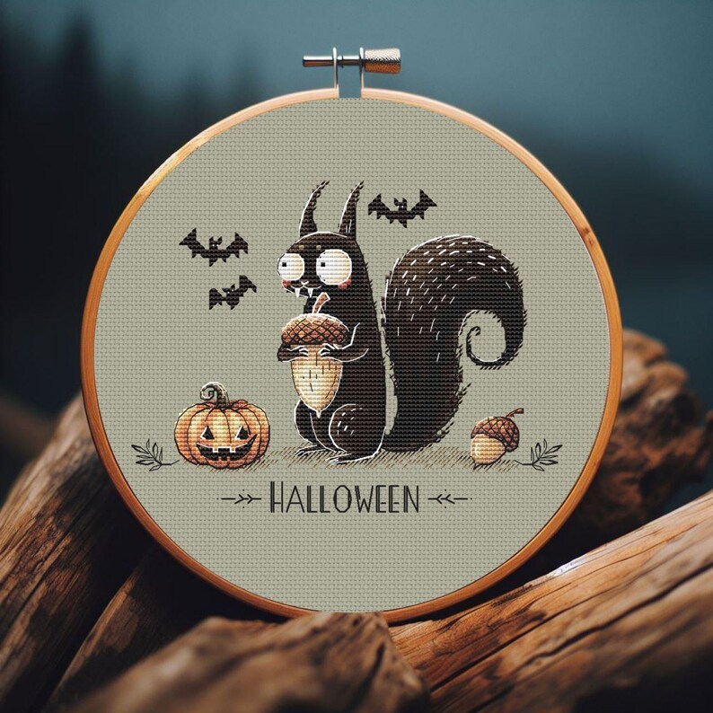May include: A Halloween-themed cross-stitch design in a wooden hoop. It features a black squirrel holding an acorn, a jack-o'-lantern, and bats. The word "HALLOWEEN" is displayed below the squirrel. The background is a muted green.