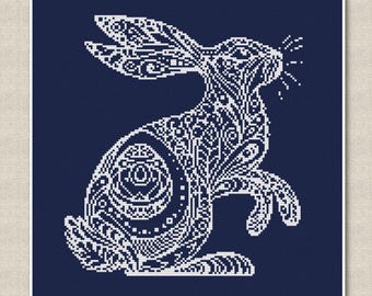 May include: A white rabbit with intricate, detailed patterns on a dark blue background. The rabbit is facing right and has its ears up. The rabbit is a stylized design with a lot of detail.