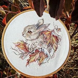 Peut inclure: Un cerceau de broderie en point de croix repr&eacute;sentant un lapin brun avec un motif de fourrure blanc et brun, entour&eacute; de feuilles d'automne color&eacute;es.