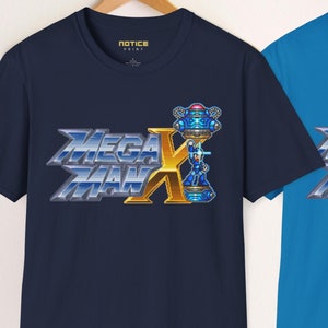 Könnte beinhalten: Drei kurzärmelige T-Shirts in Weiß, Marineblau und Türkis, jeweils mit dem Logo "Mega Man X" in Blau, Silber und Gold. Die Shirts hängen an Holzbügeln vor einer weißen Wand. Der Text "NEW STYLE!" steht oben.