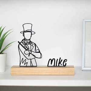Peut inclure: Silhouette noire d'un magicien avec un chapeau haut de forme et une baguette, sur une base en bois. Le nom "Mike" est également affiché en métal noir. Les articles sont affichés sur une surface blanche.