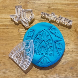 May include: A set of clear acrylic stamps for crafting. The stamps include a Texas outline, a word that says "handmade", and two decorative designs. The stamps are on a blue background.