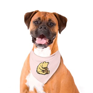 May include: A brown and white boxer dog wearing a pink bandana with a cartoon image of Winnie the Pooh holding a honey pot.