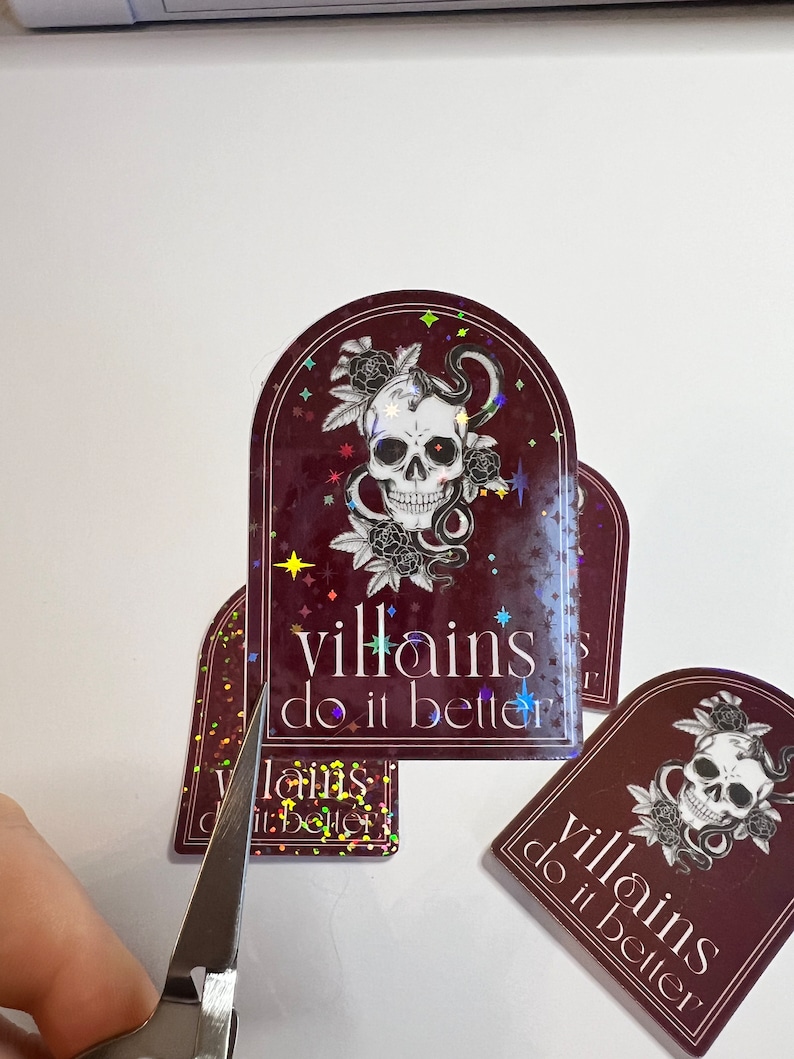 May include: A set of four holographic stickers with a skull and snake design. The stickers are burgundy with gold glitter and the text "villains do it better".