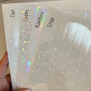 May include: Four sheets of iridescent holographic paper with different patterns: dot, gem, rainbow, and star. The paper is white with a subtle shimmer.