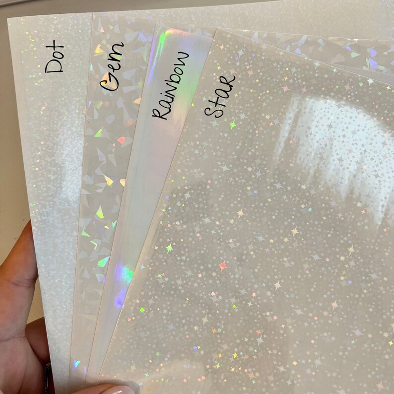 May include: Four sheets of iridescent holographic paper with different patterns: dot, gem, rainbow, and star. The paper is white with a subtle shimmer.
