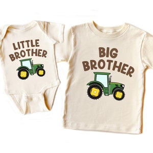 May include: Two cream colored t-shirts with a green tractor graphic and the text "Little Brother" and "Big Brother" in brown letters.
