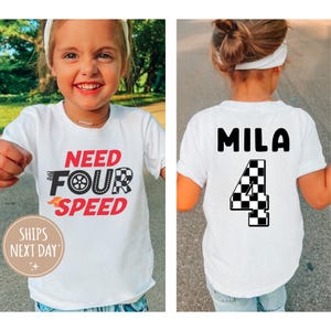 以下が含まれることがあります： 「Need Four Speed」の文字と市松模様の旗のデザインが施された白いTシャツ。Tシャツの背面には「Mila」という名前と市松模様の旗のデザインの「4」の数字が書かれています。