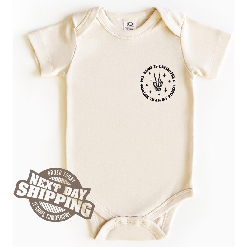 May include: A cream-coloured baby onesie with a black graphic that reads "My aunt is definitely cooler than my daddy" with a peace sign and stars.