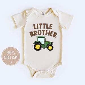 May include: A cream colored baby onesie with the text "Little Brother" in brown letters and a green tractor with yellow wheels.
