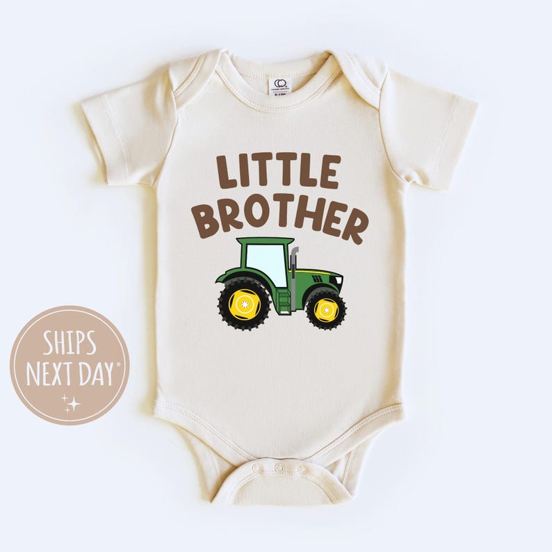 May include: A cream colored baby onesie with the text "Little Brother" in brown letters and a green tractor with yellow wheels.