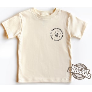 May include: A cream coloured t-shirt with a black circle graphic that says "My Aunt is Definitely Cooler Than My Daddy" with a skeleton hand making a peace sign.