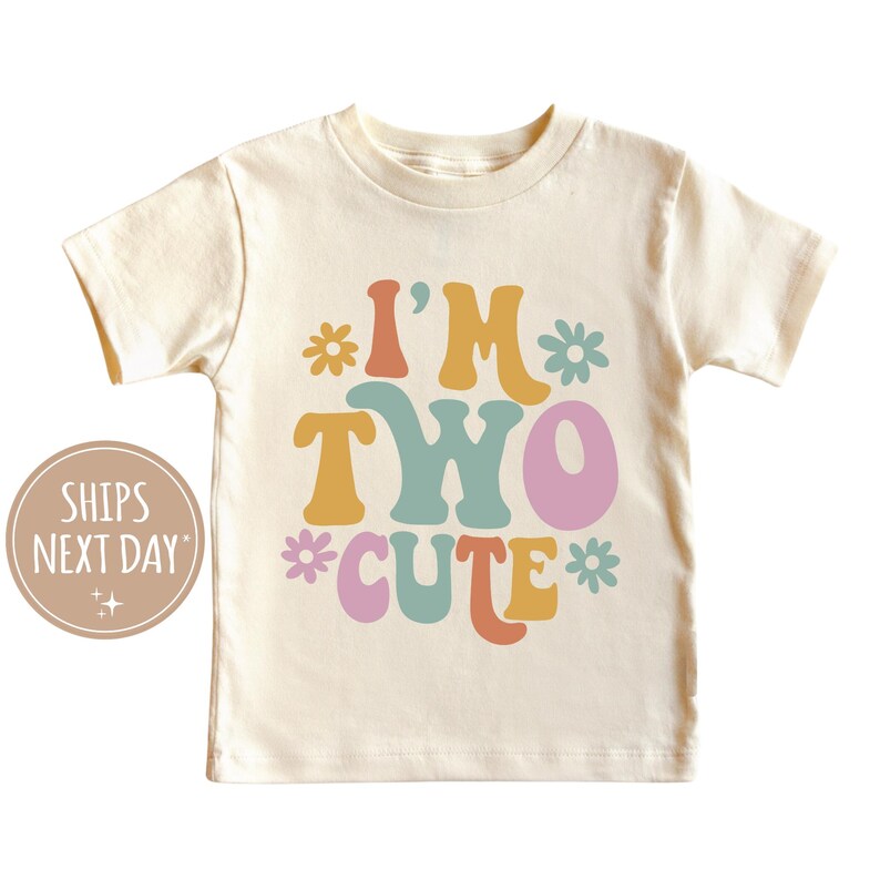 Może przedstawiać: Biała koszulka z kr&oacute;tkim rękawem z napisem "I'm Two Cute" w kolorowych, retro literach i kwiatami.