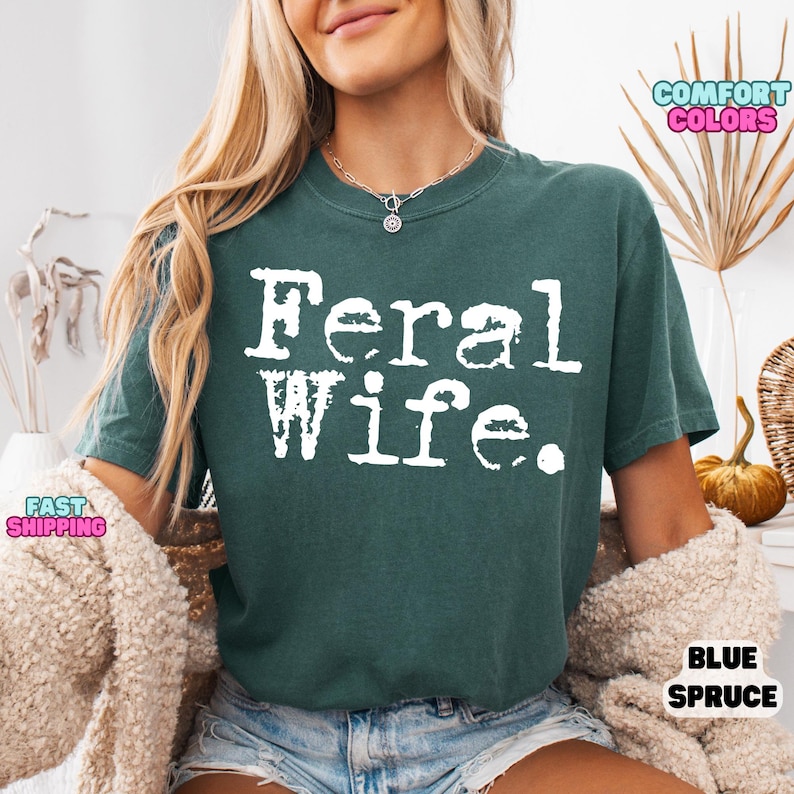 May include: A teal blue t-shirt with the text "Feral Wife." printed in white.