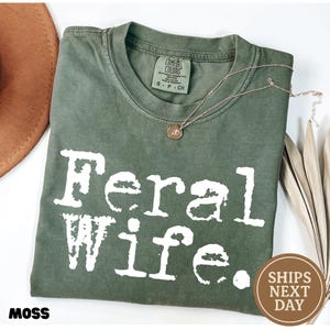May include: A green t-shirt with the text "Feral Wife." printed in white. The shirt is made of a soft, comfortable material.