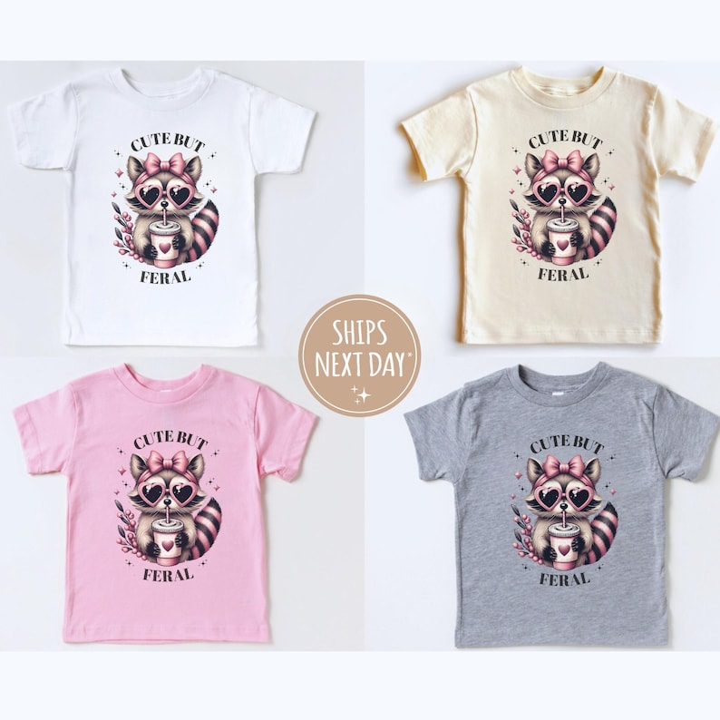 Pu&ograve; includere: Quattro magliette per bambini in bianco, beige, rosa e grigio, ognuna con una grafica di procione. Il procione indossa occhiali da sole e un fiocco, tenendo in mano una tazza. Il testo recita "CUTE BUT FERAL."