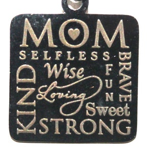 May include: A black metal pendant necklace with a silver chain. The pendant is rectangular and features the word "MOM" with a heart in the center. The words "SELFLESS, WISE, LOVING, KIND, STRONG, SWEET, FUN, BRAVE" are arranged around the word "MOM".