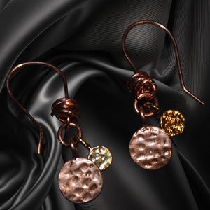 May include: A pair of copper and gold earrings with a hammered copper disc and a smaller gold disc. The earrings are hanging from a copper wire loop.