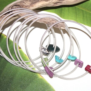 May include: A set of silver bangle bracelets with colorful stone accents. The bracelets are stacked on top of each other, creating a layered look. The stones are in various shapes and sizes, including a heart, a square, and a teardrop.