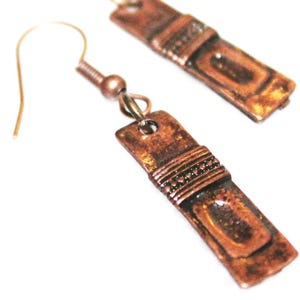 May include: A pair of copper earrings with a textured, rectangular design. The earrings have a simple, wire hook closure.