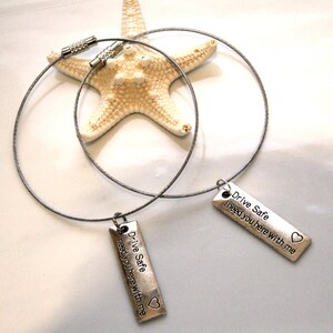May include: Two silver keychains with a silver cable chain. Each keychain has a silver rectangular tag with the text "Drive Safe I need you here with me" and a small heart symbol.