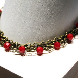 May include: A gold chain necklace with red glass beads. The necklace is layered and has a delicate look.