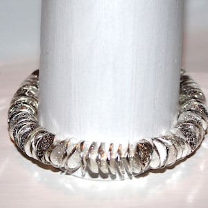 May include: A silver bracelet made of small, round, overlapping pieces. The bracelet has a sparkly, textured finish.