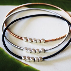 May include: Three stacked bracelets made of black, silver, and copper wire with silver cube beads.