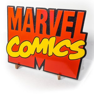 May include: A red and yellow sign with the words "MARVEL COMICS" in black lettering. The sign is made of a glossy material and has a 3D effect.