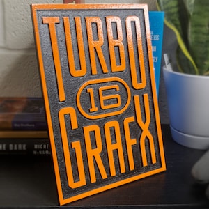 May include: A black and orange wooden sign with the text "TURBO 16 GRAFX" in a bold, stylized font.