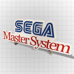 May include: A white plastic sign with the words "SEGA Master System" in blue and red letters. The letters are raised and have a textured surface.