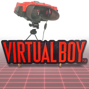 Könnte beinhalten: Ein rotes und schwarzes Virtual Boy-Spielekonsole mit einem schwarzen Ständer und einem roten und schwarzen Schild mit der Aufschrift "VIRTUAL BOY" mit einem Warenzeichen.