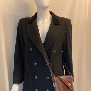 May include: A black double-breasted wool coat with a brown leather shoulder bag. The coat has a velvet collar and six buttons down the front.