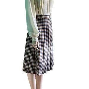 May include: A cream-colored blouse with long sleeves and a high collar paired with a knee-length pleated skirt. The skirt features a brown, navy, and white plaid pattern. The outfit is displayed on a mannequin.