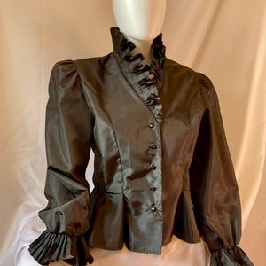 May include: A black satin blouse with a ruffled collar and cuffs. The blouse has a fitted bodice and a peplum hem.