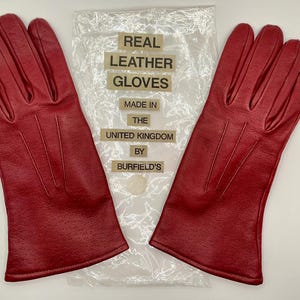Puede incluir: Un par de guantes de cuero rojo brillante con un dise&ntilde;o perforado. Los guantes est&aacute;n hechos en el Reino Unido y se muestran con el embalaje original. El embalaje dice "Real Leather Gloves".