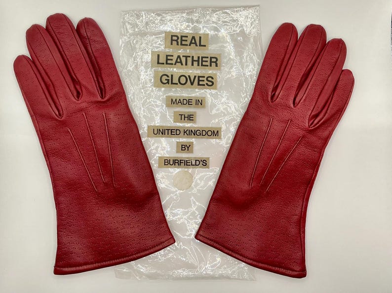 Puede incluir: Un par de guantes de cuero rojo brillante con un dise&ntilde;o perforado. Los guantes est&aacute;n hechos en el Reino Unido y se muestran con el embalaje original. El embalaje dice "Real Leather Gloves".