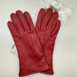 Puede incluir: Un par de guantes de cuero rojo brillante. Los guantes tienen un dise&ntilde;o perforado y est&aacute;n empaquetados en una bolsa de pl&aacute;stico transparente. Los guantes son de un tono rojo vibrante.