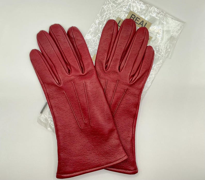 Puede incluir: Un par de guantes de cuero rojo brillante. Los guantes tienen un dise&ntilde;o perforado y est&aacute;n empaquetados en una bolsa de pl&aacute;stico transparente. Los guantes son de un tono rojo vibrante.